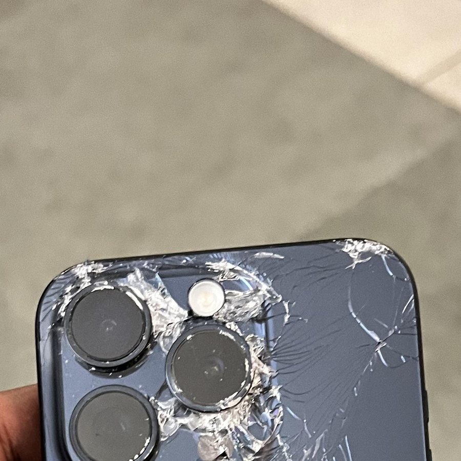The back of a dark iPhone, glass shattered around the cameras.